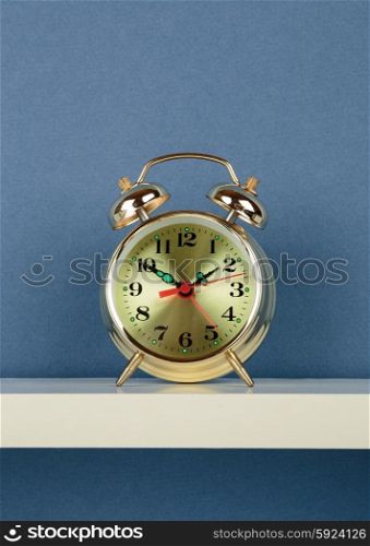 alarm clock on white shelf on blue wallpaper background