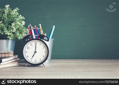Alarm clock on wooden table on blackboard background in classroom,back to school concept