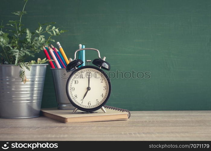 Alarm clock on wooden table on blackboard background in classroom,back to school concept