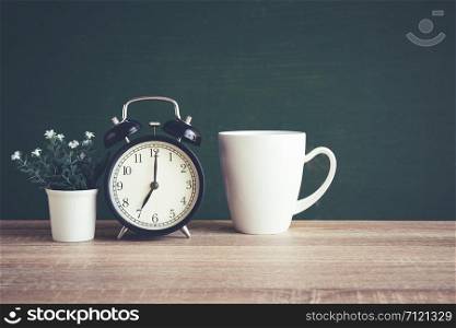 Alarm clock on wooden table on blackboard background in classroom, Back to school concept