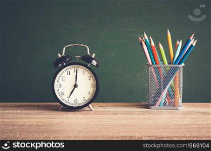Alarm clock on wooden table on blackboard background in classroom, Back to school concept