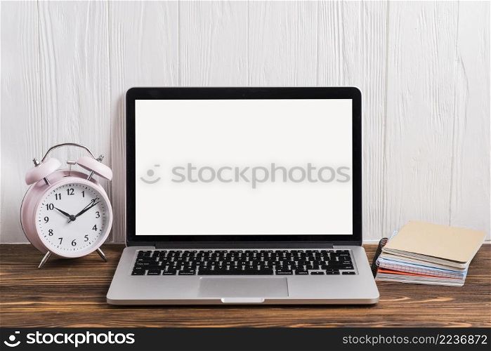 alarm clock open laptop notebook stacked wooden desk against wall