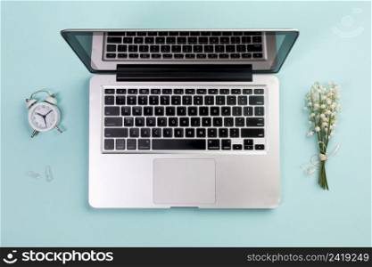 alarm clock paper clip lily valley bouquet with open laptop blue business desk