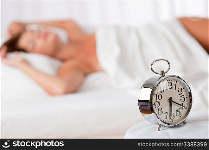 Alarm clock standing on white bed woman in background