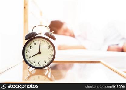 Alarm clock with sleeping woman in bed room. Lazy time in holiday concept.