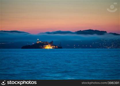Alcatraz Island at sunset surrounded by fog and mountains.