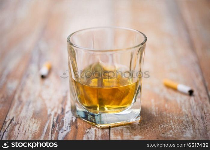 alcohol addiction and alcoholism concept - close up of glass of whiskey and cigarette butts on table. glass of alcohol on table and cigarette butts. glass of alcohol on table and cigarette butts