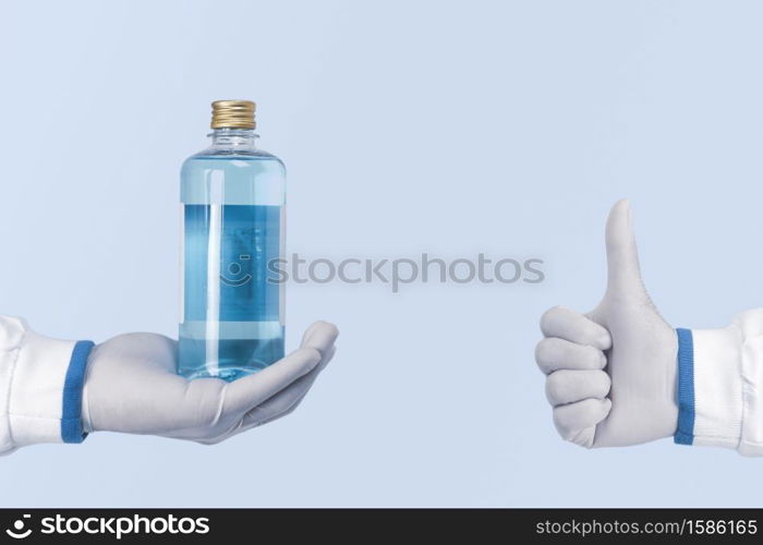 Alcohol antiseptic and disinfectant bottle in a hand and showing thumb up of healthcare workers on blue color background