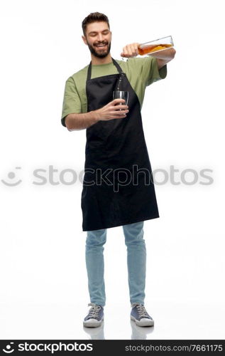 alcohol drinks, people and job concept - happy smiling barman in black apron with shaker and glass bottle preparing cocktail over white background. barman with bottle and shaker preparing drink
