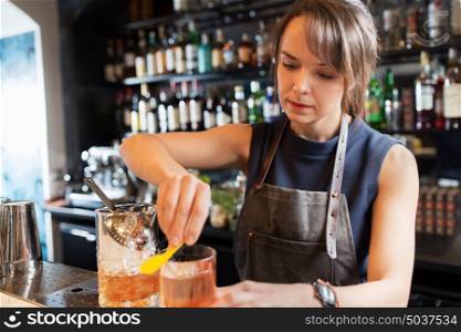 alcohol drinks, people and luxury concept - barmaid with glass and jug preparing cocktail at bar. barmaid with glass and jug preparing cocktail