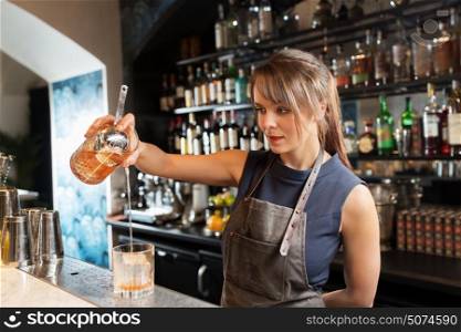 alcohol drinks, people and luxury concept - barmaid with glass and jug preparing cocktail at bar. barmaid with glass and jug preparing cocktail