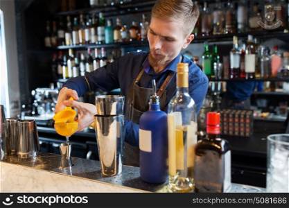 alcohol drinks, people and luxury concept - barman with shaker and bottles squeezing juice into jigger and preparing cocktail at bar. barman with shaker, alcohol and jigger at bar