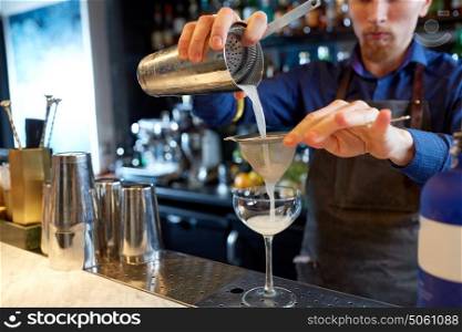 alcohol drinks, people and luxury concept - bartender pouring cocktail from shaker through strainer into glass at bar. bartender with shaker preparing cocktail at bar