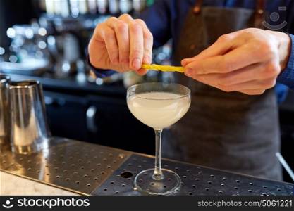 alcohol drinks, people and luxury concept - bartender with glass and lemon peel preparing cocktail at bar. bartender with glass of cocktail and lemon at bar