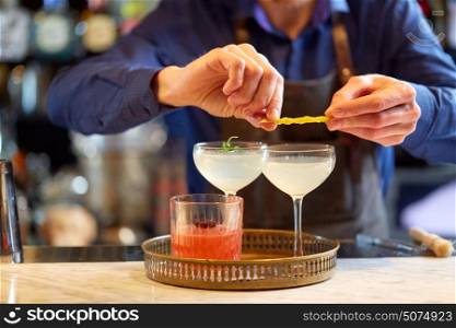 alcohol drinks, people and luxury concept - bartender with glasses and lemon peel preparing cocktail at bar. bartender with glass of cocktail and lemon at bar