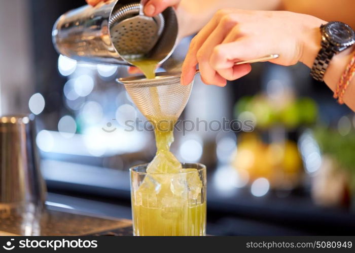 alcohol drinks, people and luxury concept - close up of woman bartender hands pouring cocktail from shaker to glass at bar. close up of bartender preparing cocktail at bar