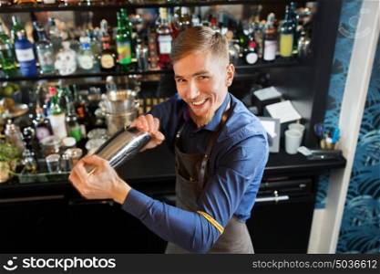 alcohol drinks, people and luxury concept - happy smiling barman with shaker preparing cocktail at bar. happy barman with shaker preparing cocktail at bar