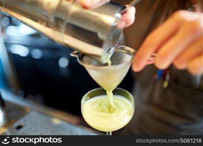 alcohol drinks, people and luxury concept - woman bartender poring cocktail from shaker through strainer into glass at bar. bartender pouring cocktail into glass at bar