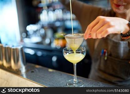 alcohol drinks, people and luxury concept - woman bartender poring cocktail through strainer into glass at bar. bartender pouring cocktail into glass at bar