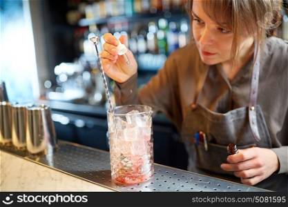 alcohol drinks, people and luxury concept - woman bartender preparing cocktail and adding essence into glass with ice at bar counter. bartender adding essence to cocktail glass at bar