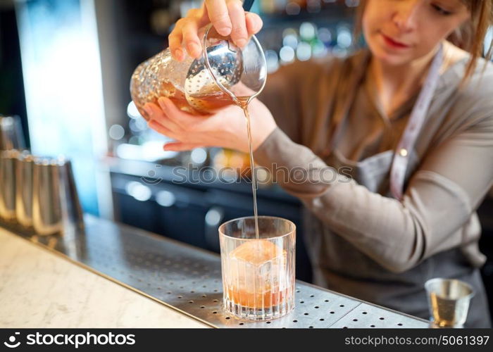 alcohol drinks, people and luxury concept - woman bartender with glass and jug preparing cocktail at bar. bartender with glass and jug preparing cocktail