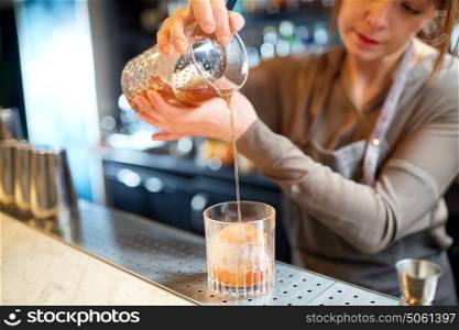 alcohol drinks, people and luxury concept - woman bartender with glass and jug preparing cocktail at bar. bartender with glass and jug preparing cocktail