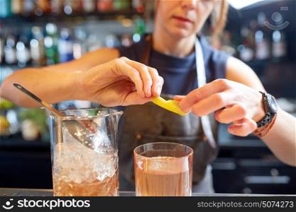 alcohol drinks, people and luxury concept - woman bartender with glass and jug preparing cocktail at bar. bartender with glass of cocktail and lemon at bar
