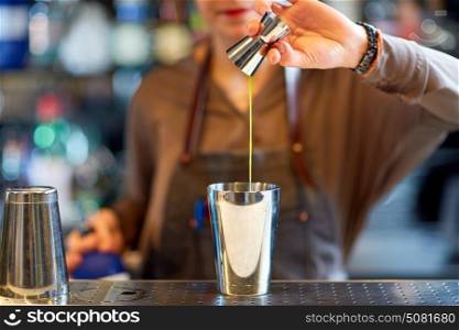 alcohol drinks, people and luxury concept - woman bartender with jigger pouring syrup into shaker and preparing cocktail at bar counter. bartender with cocktail shaker and jigger at bar