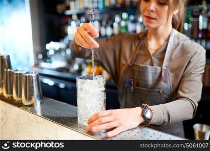 alcohol drinks, people and luxury concept - woman bartender with stirrer and glass of ice preparing cocktail at bar counter. bartender with cocktail stirrer and glass at bar