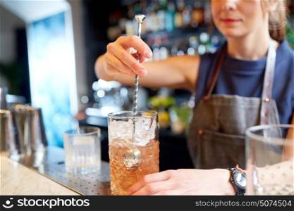 alcohol drinks, people and luxury concept - woman bartender with stirrer and glass preparing cocktail at bar counter. bartender with cocktail stirrer and glass at bar