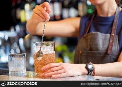 alcohol drinks, people and luxury concept - woman bartender with stirrer and glass preparing cocktail at bar counter. bartender with cocktail stirrer and glass at bar