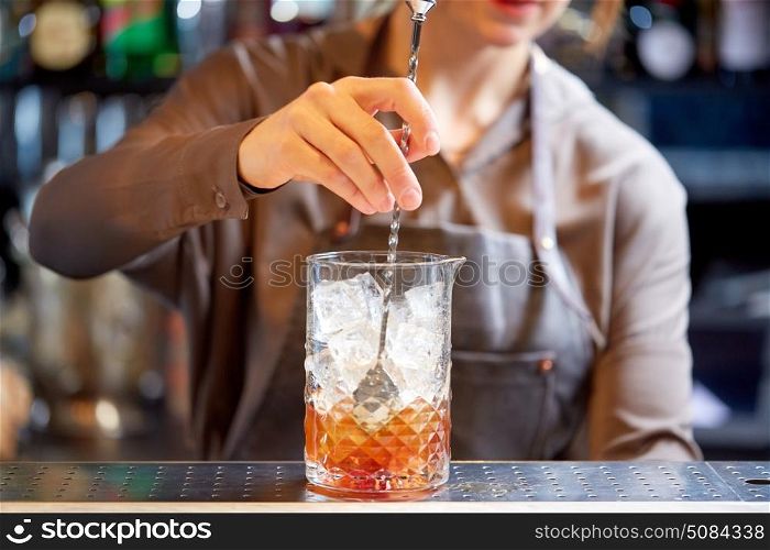 alcohol drinks, people and luxury concept - woman bartender with stirrer and glass preparing cocktail at bar counter. bartender with cocktail stirrer and glass at bar. bartender with cocktail stirrer and glass at bar