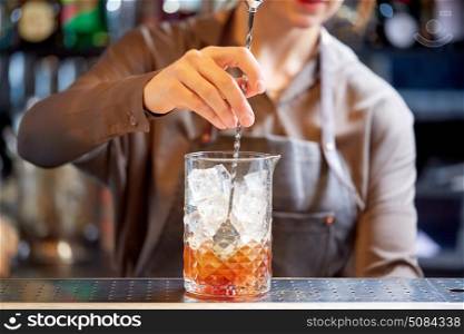 alcohol drinks, people and luxury concept - woman bartender with stirrer and glass preparing cocktail at bar counter. bartender with cocktail stirrer and glass at bar. bartender with cocktail stirrer and glass at bar