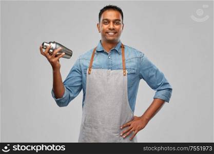 alcohol drinks, people and profession concept - indian barman in apron with cocktail shaker over grey background. indian barman in apron with cocktail shaker