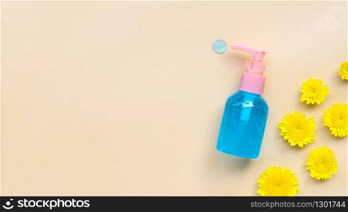 Alcohol hand sanitizer gel in pump bottle with yellow flower on cream color background. Copy space