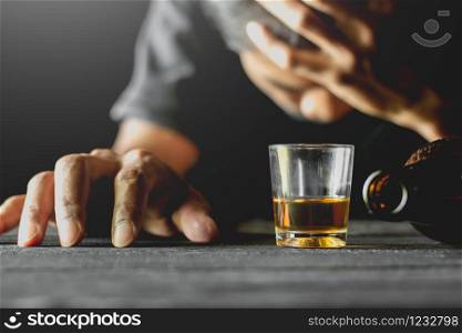 Alcohol in a small glass is placed on a black table while a man is sitting in a drunken state.