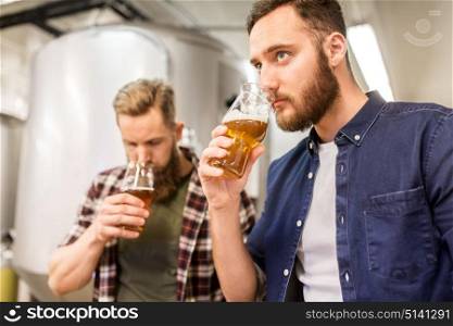 alcohol production, business and people concept - men drinking and testing craft beer at brewery. men drinking and testing craft beer at brewery