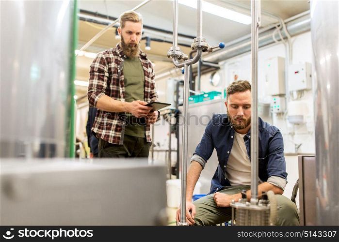 alcohol production, business and people concept - men with tablet pc computer at craft beer brewery filter. men with tablet pc at craft beer brewery filter