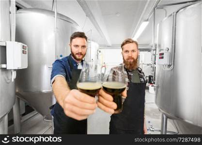 alcohol production, manufacture, business and people concept - male brewers clinking glasses of craft beer at brewery. brewers clinking glasses of craft beer at brewery