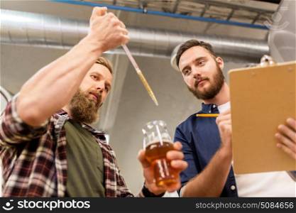 alcohol production, manufacture, business and people concept - men with pipette and clipboard testing craft beer at brewery. men with pipette testing craft beer at brewery. men with pipette testing craft beer at brewery