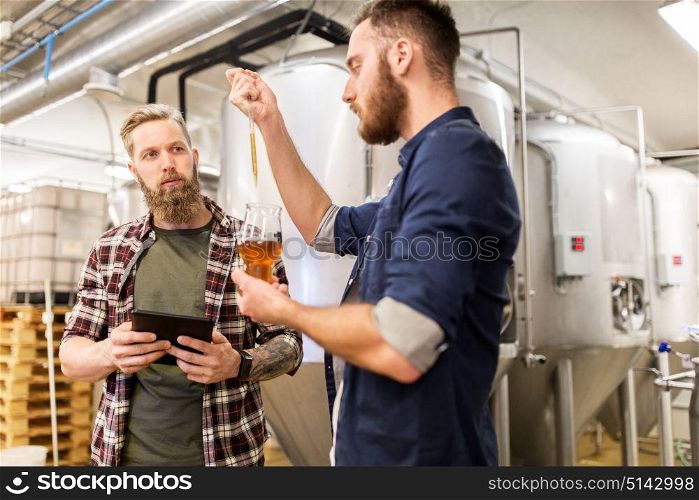 alcohol production, manufacture, business and people concept - men with pipette and tablet pc computer testing craft beer at brewery. men with pipette testing craft beer at brewery