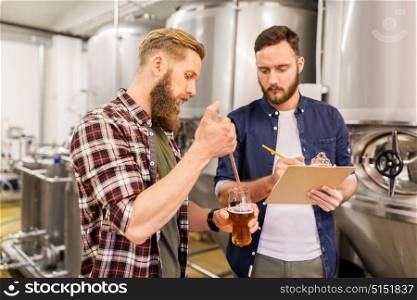 alcohol production, manufacture, business and people concept - men with pipette and clipboard testing craft beer at brewery. men with pipette testing craft beer at brewery