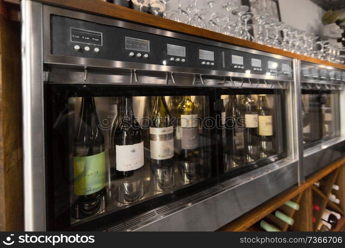 alcohol, technology and storage concept - close up of wine bottles storing in dispenser at bar or restaurant. close up of wine bottles in dispenser at bar