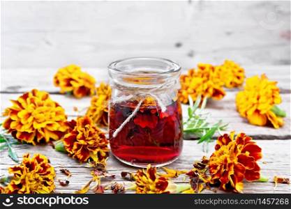 Alcohol tincture of marigolds in a glass jar, fresh and dried flowers with green leaves on wooden board background