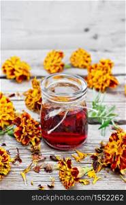 Alcohol tincture of marigolds in a glass jar, fresh and dried flowers on wooden board background