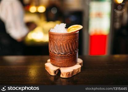 Alcoholic beverage with lemon and ice in wooden cup closeup.