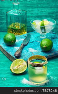 alcoholic cocktail with lime. Glass with alcohol and fruits of lime and the bowl with ice on wooden background