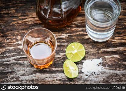 alcoholic drinks and lemon salt on rustic wood background / brandy in a glass with alcohol bottles and water - vodka rum cognac tequila and whiskey concept