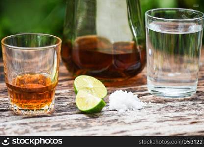 alcoholic drinks and lemon salt on rustic wood background / brandy in a glass with alcohol bottles and water - vodka rum cognac tequila and whiskey concept