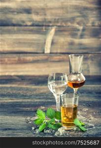 Alcoholic drinks with ice and mint leaves on wooden background. Vintage style toned picture